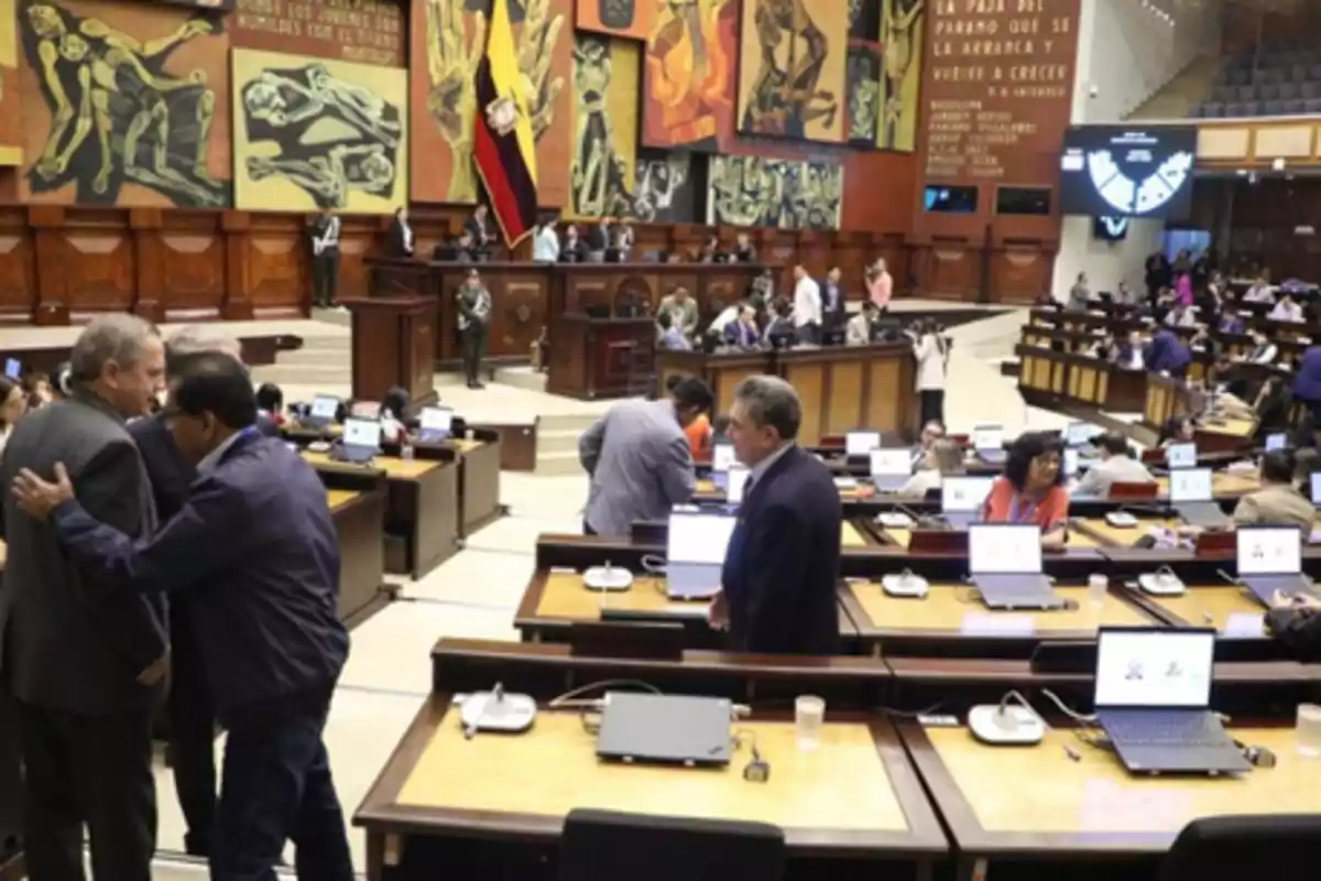 Personas trabajando y conversando en el interior de un parlamento con computadoras portátiles sobre los escritorios y murales artísticos en las paredes