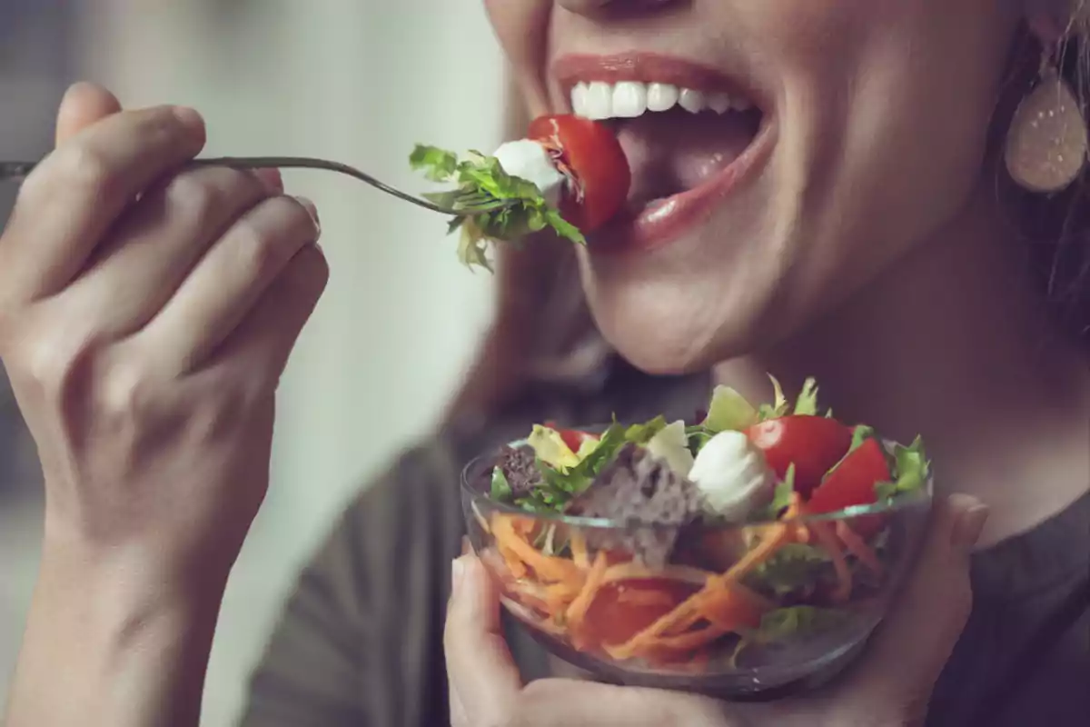 Mujer sonriente comiendo una ensalada fresca con tomate, zanahoria y lechuga Mujer sonriente comiendo una ensalada fresca con tomate, zanahoria y lechuga