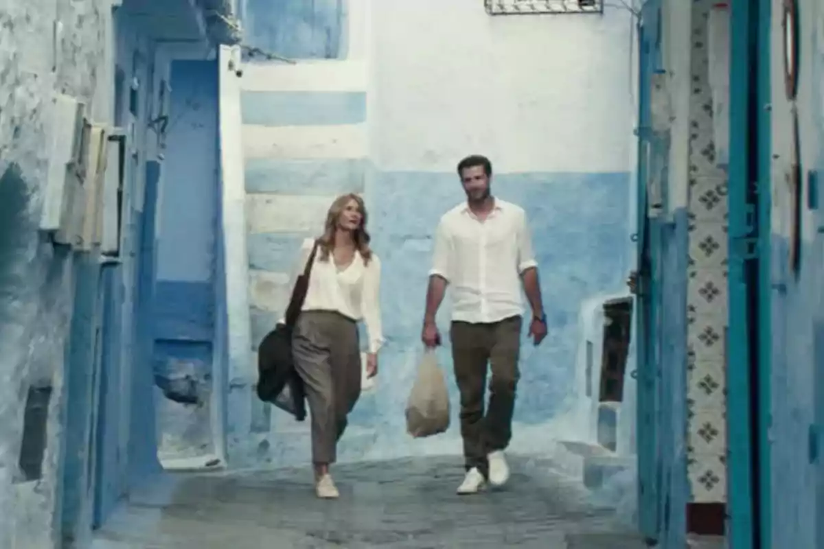 A couple walks down a narrow street with blue and white painted walls in a Mediterranean setting. A couple walks down a narrow street with blue and white painted walls in a Mediterranean setting.
