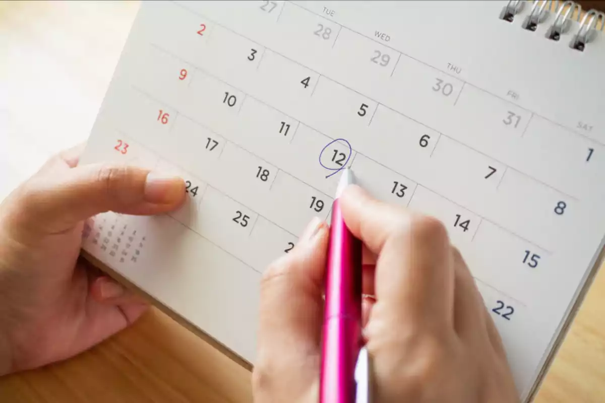Person marking the 12th on a calendar with a pink pen