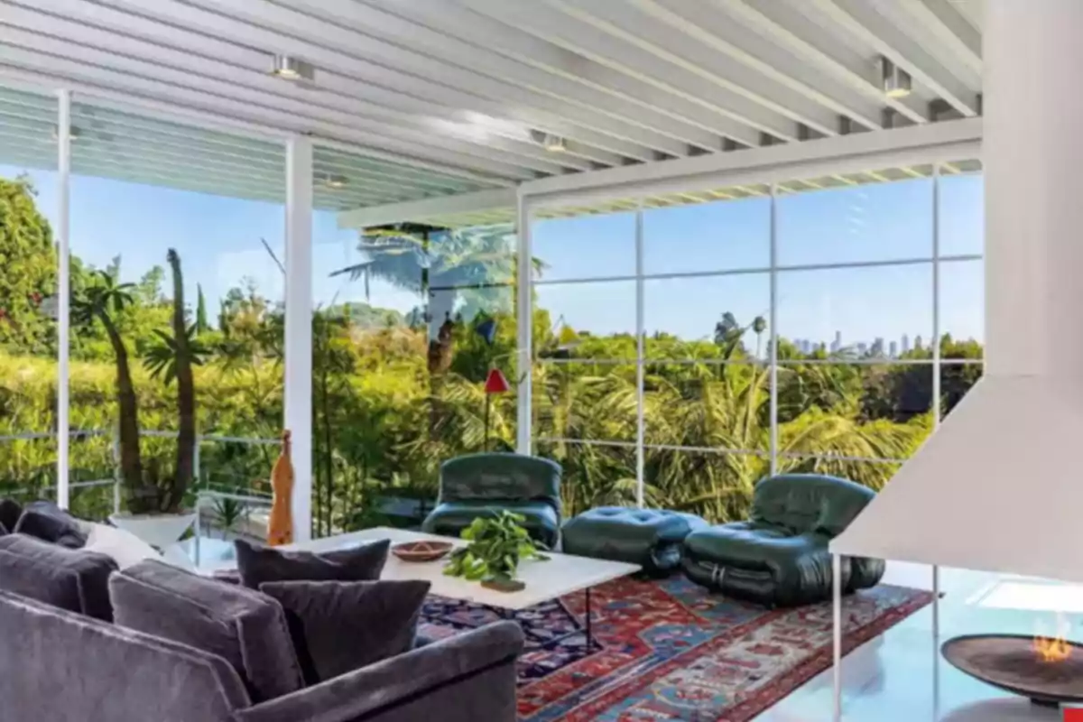 Modern living room with large windows, comfortable furniture, colorful rug, and a view of a garden full of plants and palm trees Modern living room with large windows, comfortable furniture, colorful rug, and a view of a garden full of plants and palm trees