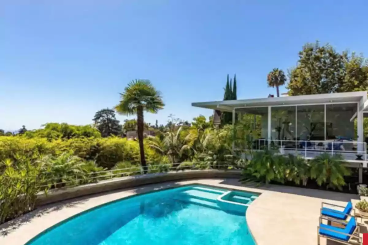 Modern house with large windows and a pool surrounded by greenery and palm trees on a sunny day Modern house with large windows and a pool surrounded by greenery and palm trees on a sunny day