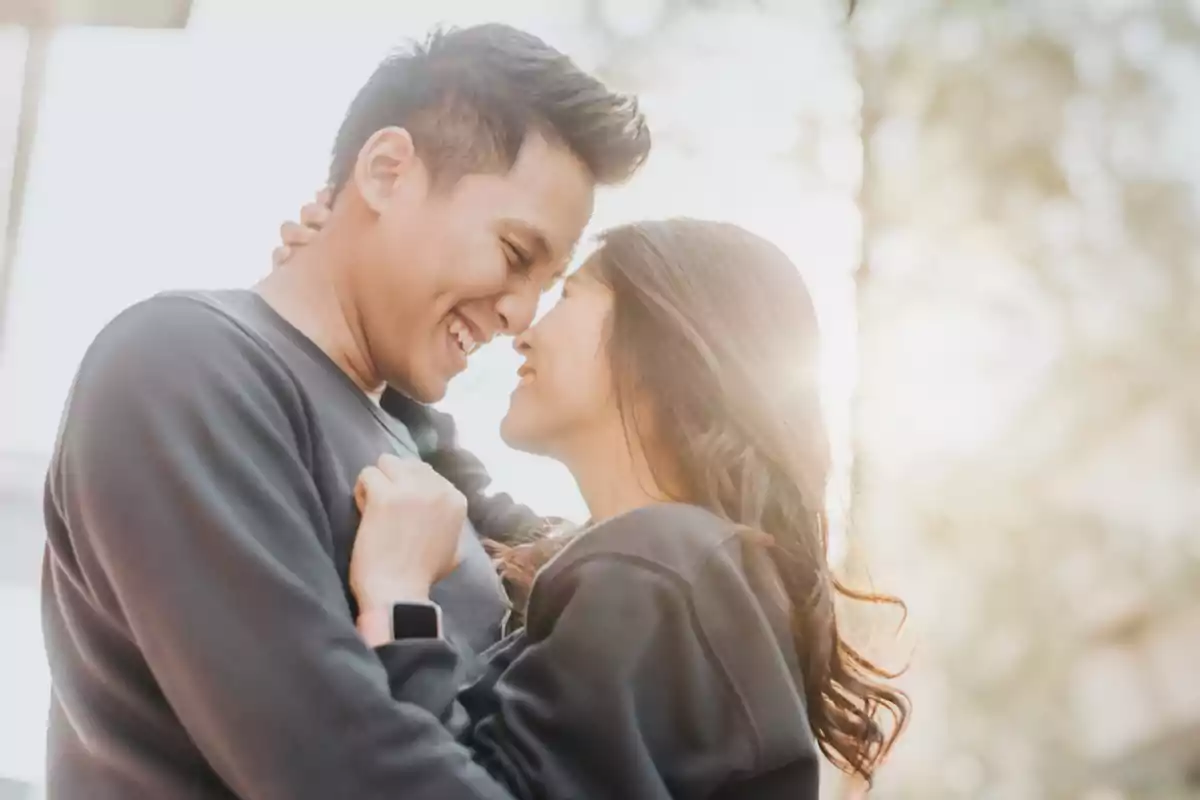 Pareja joven abrazándose y sonriendo al aire libre con luz de sol de fondo Pareja joven abrazándose y sonriendo al aire libre con luz de sol de fondo