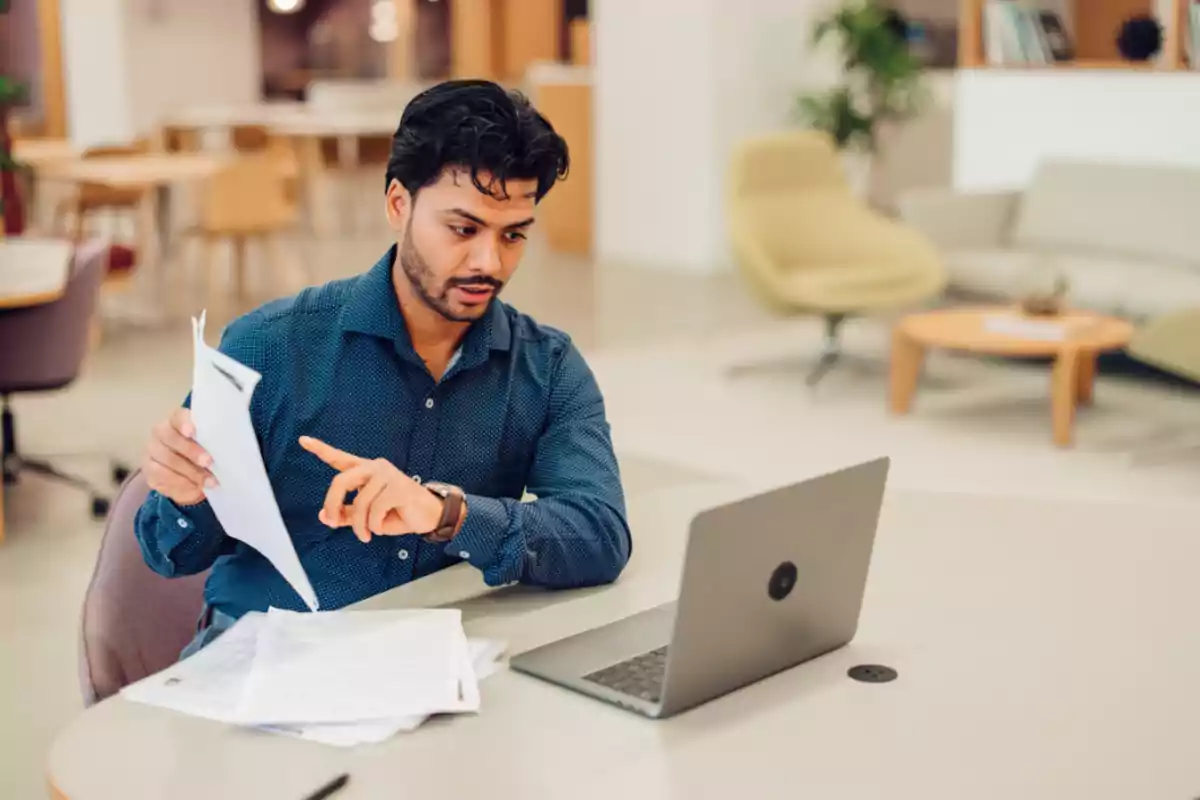 Hombre sentado en una oficina revisando documentos mientras trabaja en una computadora portátil Hombre sentado en una oficina revisando documentos mientras trabaja en una computadora portátil