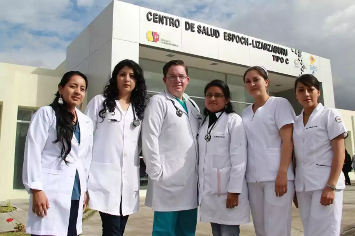 Grupo de profesionales de la salud con batas blancas posando frente a un centro de salud llamado Centro de Salud ESPOCH-Lizarzaburu Grupo de profesionales de la salud con batas blancas posando frente a un centro de salud llamado Centro de Salud ESPOCH-Lizarzaburu