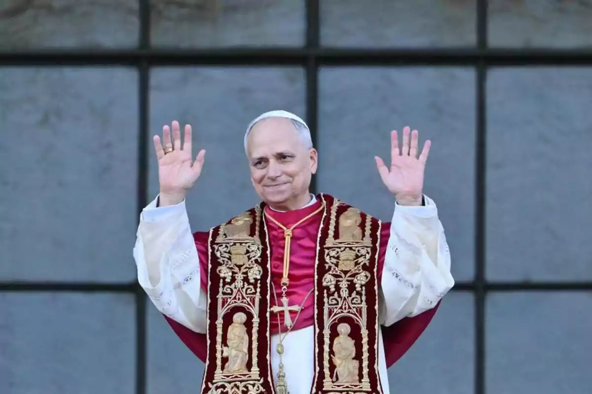 Man dressed in papal attire raising both hands in front of a large window
