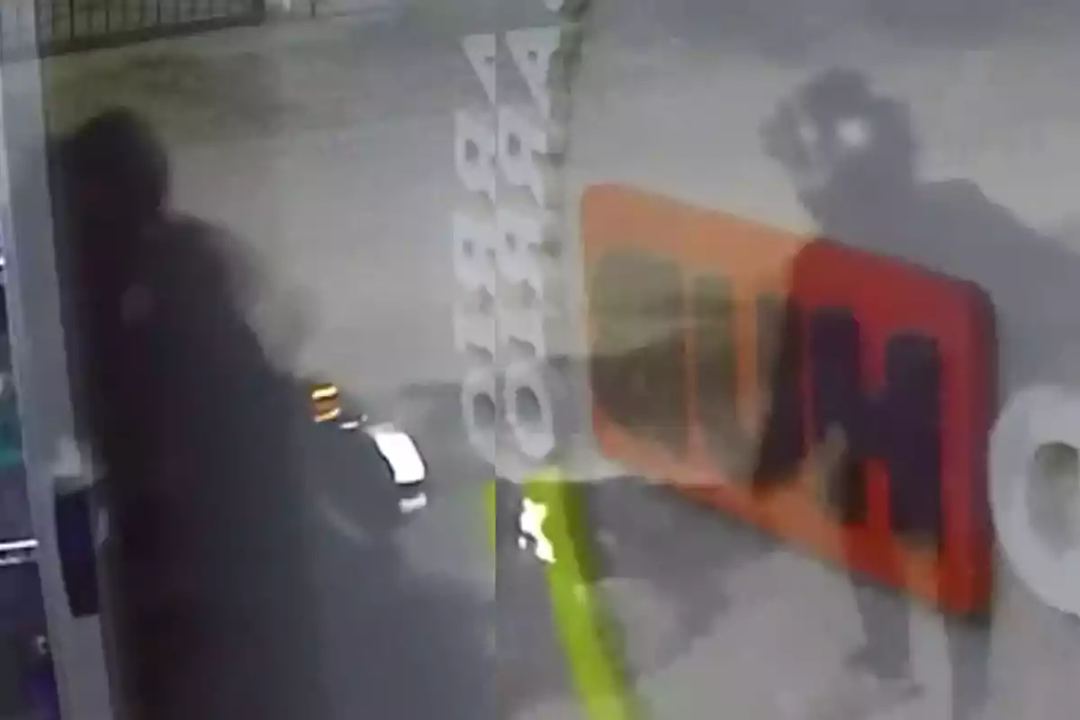 Blurry image from a security camera showing the silhouette of a person next to a motorcycle in front of an establishment with signs reflected in the glass.