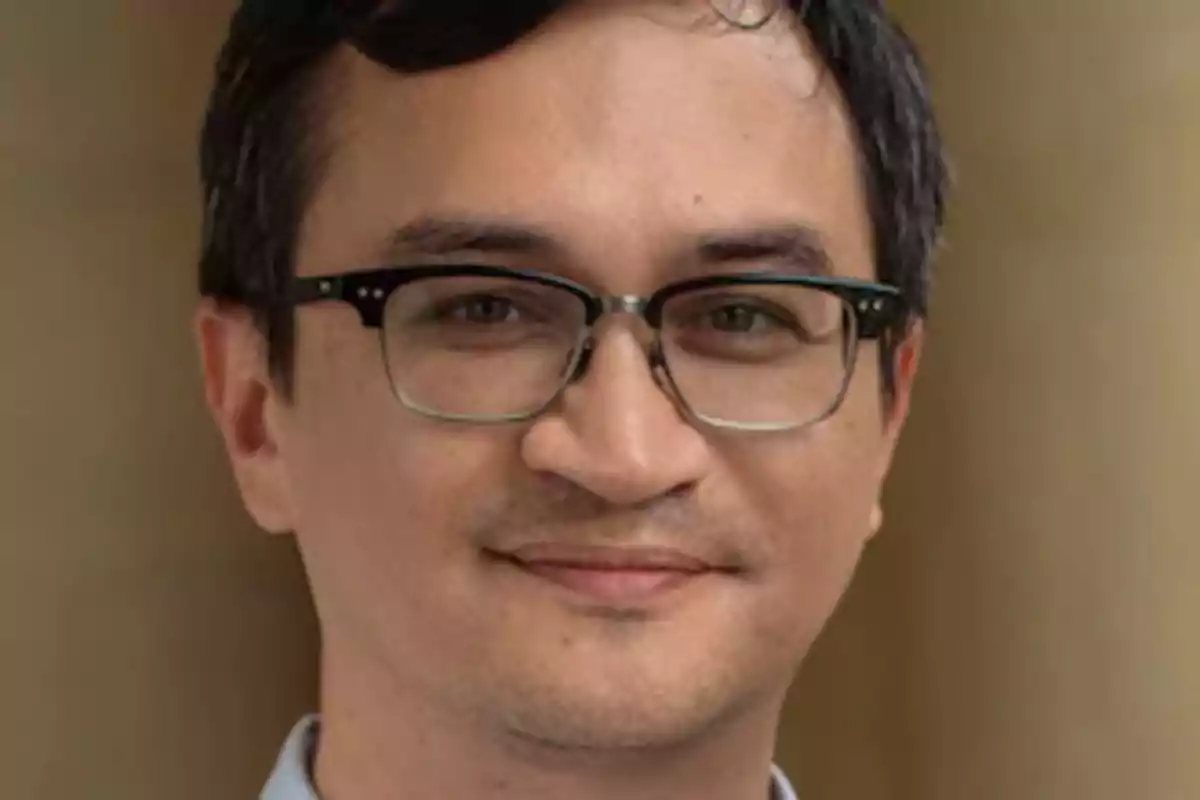 Hombre joven con gafas y cabello oscuro mirando a la cámara con una ligera sonrisa