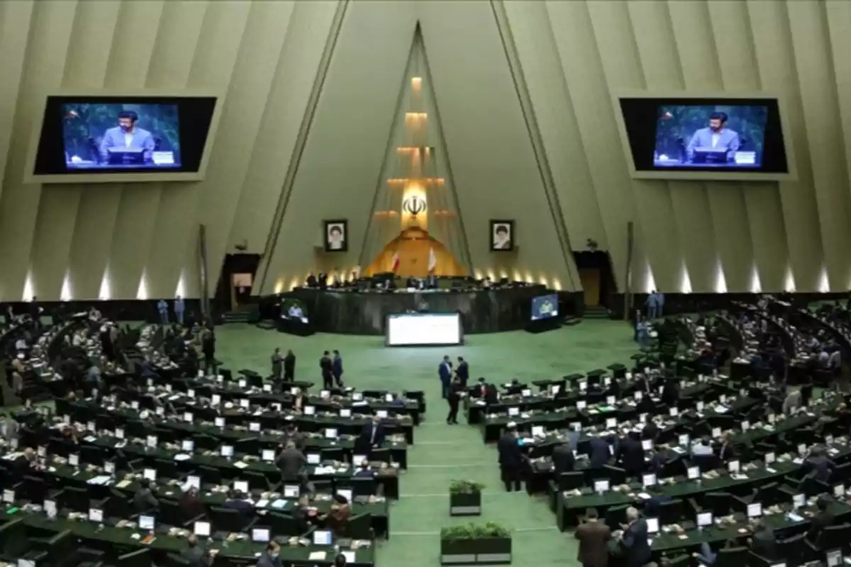 Overview of the interior of a parliament with numerous seats occupied by people and a large screen displaying a speaker Overview of the interior of a parliament with numerous seats occupied by people and a large screen displaying a speaker