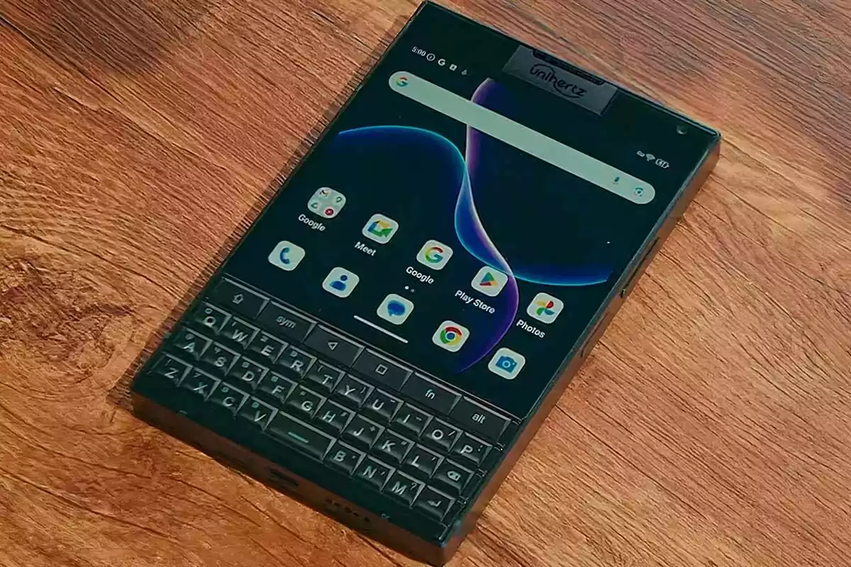 Teléfono inteligente con teclado físico y pantalla táctil encendido sobre una superficie de madera Teléfono inteligente con teclado físico y pantalla táctil encendido sobre una superficie de madera