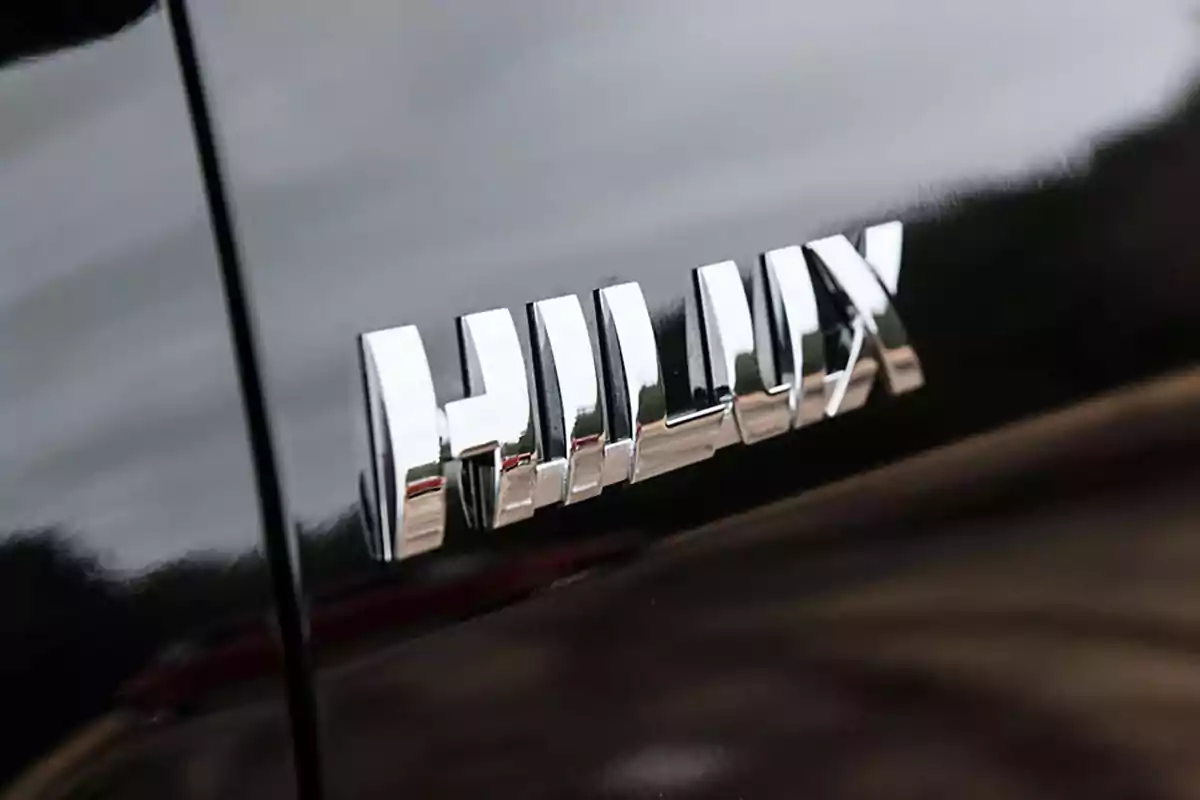 Emblema cromado de la palabra Hilux sobre la carrocería de un vehículo negro Emblema cromado de la palabra Hilux sobre la carrocería de un vehículo negro