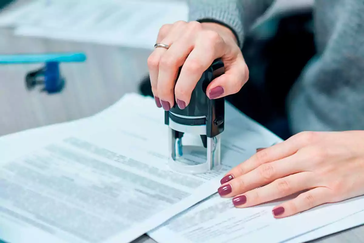 Manos de una persona sellando documentos oficiales en una oficina Manos de una persona sellando documentos oficiales en una oficina