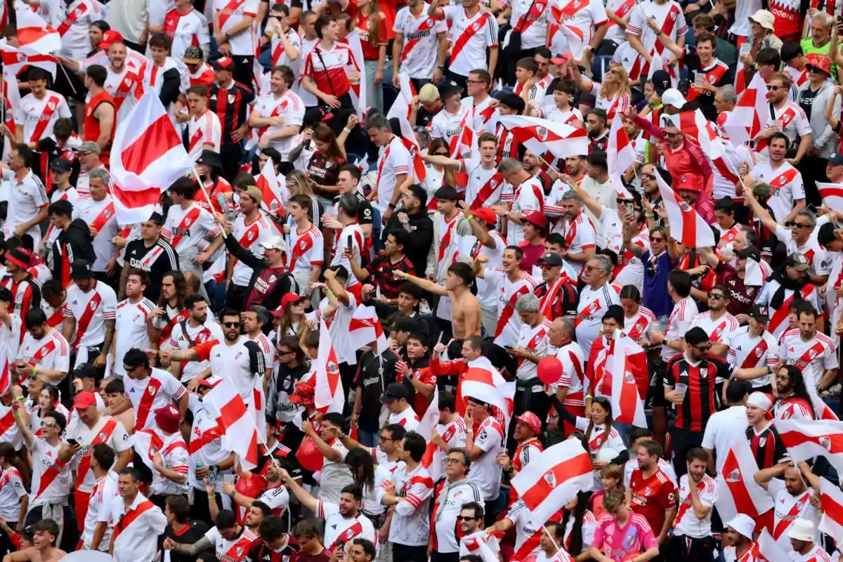Aficionados de River Plate animando en las gradas con camisetas y banderas blancas y rojas