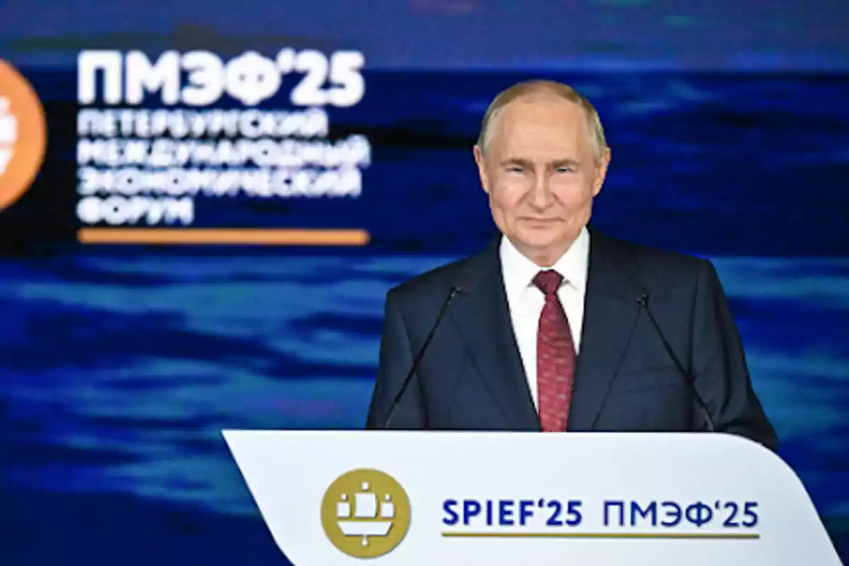 Man in a dark suit and red tie speaking at a podium during an international economic forum in St. Petersburg with a blue background and letters in Russian and English Man in a dark suit and red tie speaking at a podium during an international economic forum in St. Petersburg with a blue background and letters in Russian and English