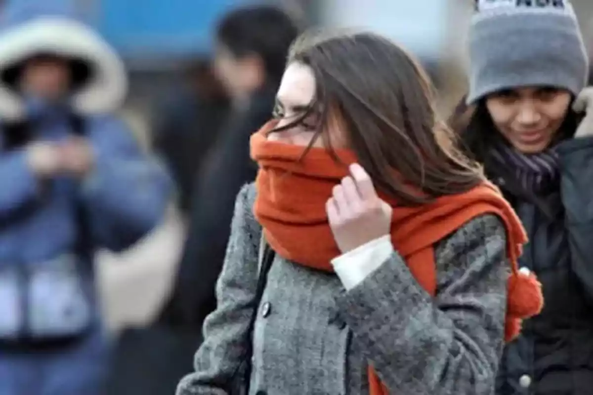 Mujer joven abrigada con bufanda naranja y abrigo gris caminando en un día frío Mujer joven abrigada con bufanda naranja y abrigo gris caminando en un día frío