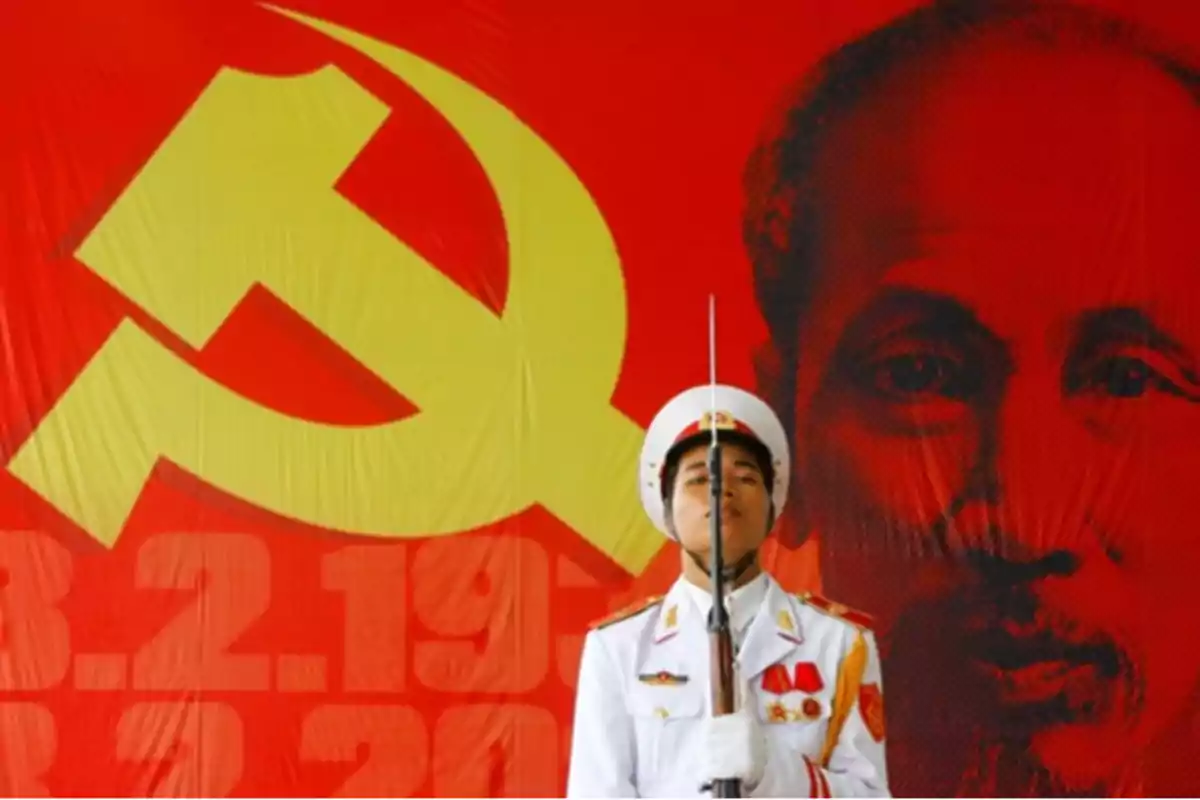 Un soldado con uniforme blanco y rifle está de pie frente a un fondo rojo con la hoz y el martillo y el retrato de un hombre. Un soldado con uniforme blanco y rifle está de pie frente a un fondo rojo con la hoz y el martillo y el retrato de un hombre.
