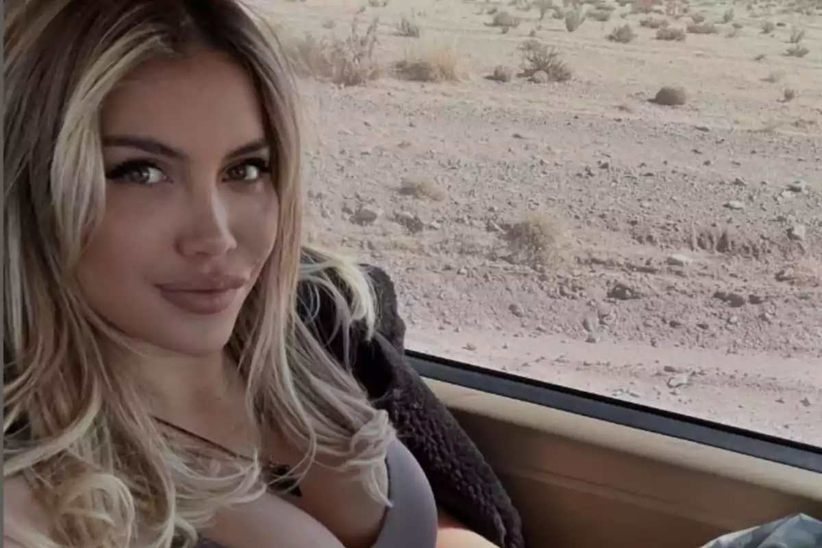 Mujer de cabello rubio sentada dentro de un auto con paisaje desértico al fondo