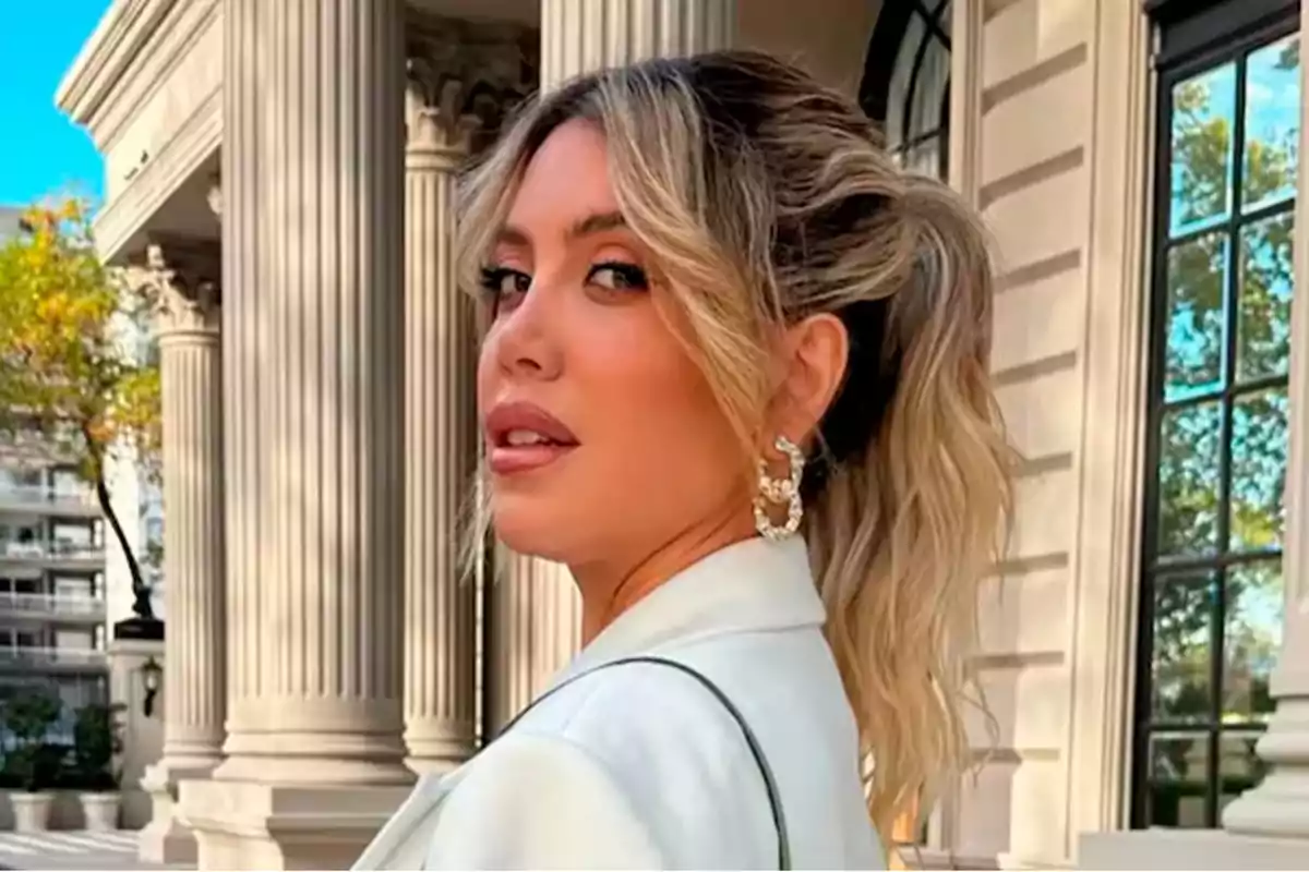 Mujer rubia con el cabello recogido y chaqueta clara posando frente a un edificio elegante con columnas