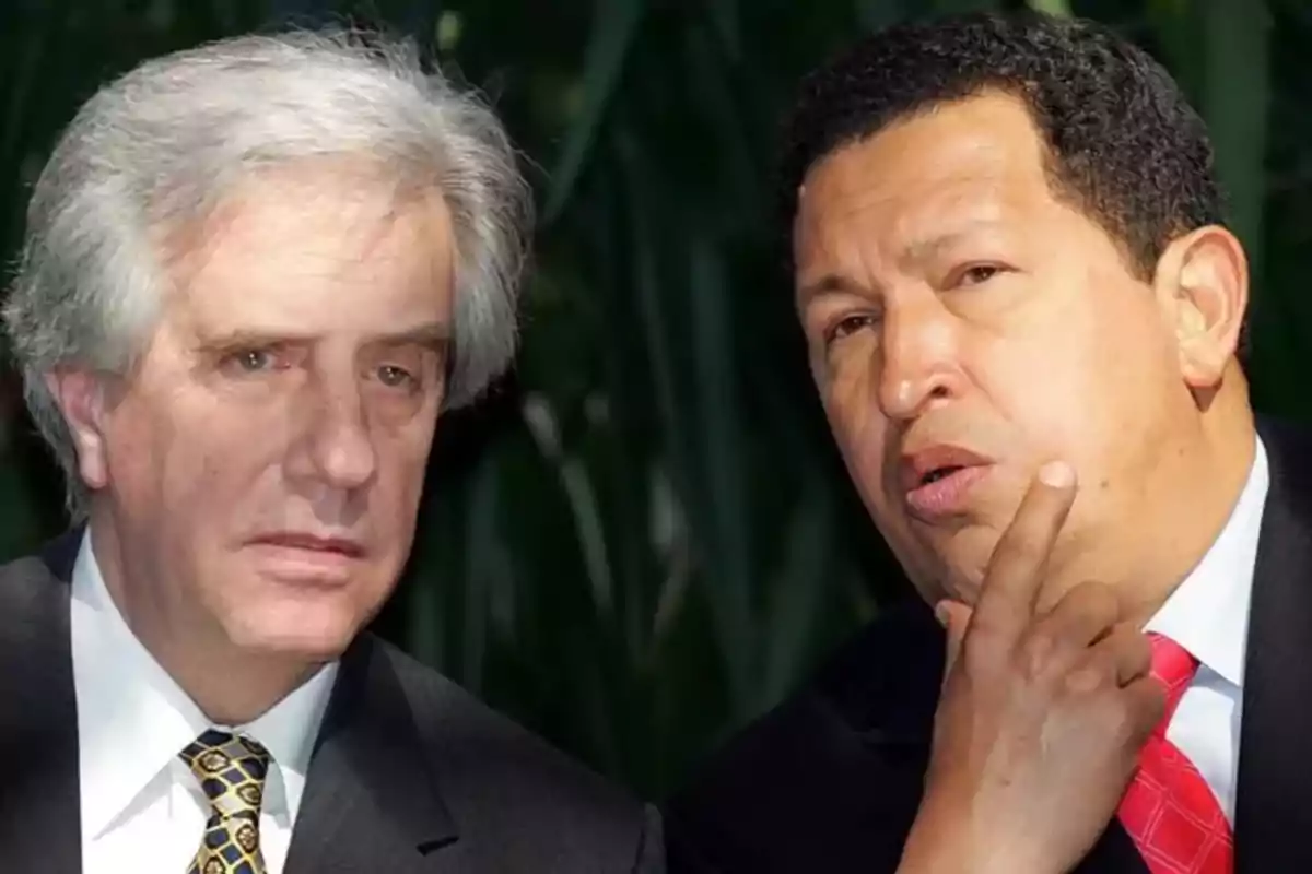 Two men in suits are talking outdoors with vegetation in the background.