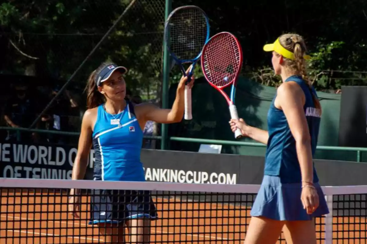 Two tennis players greet each other by tapping their rackets on a clay court at the end of a match.