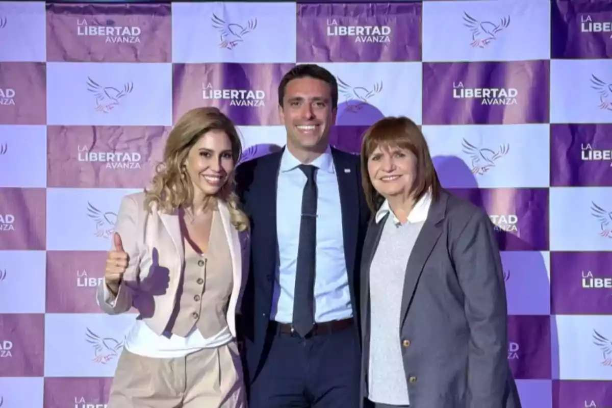 Tres personas posan sonrientes frente a un fondo con el logo y el texto La Libertad Avanza