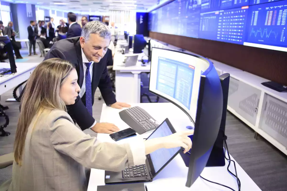 Dos personas en una oficina moderna observan y analizan información en una pantalla curva de computadora rodeados de monitores y gráficos digitales