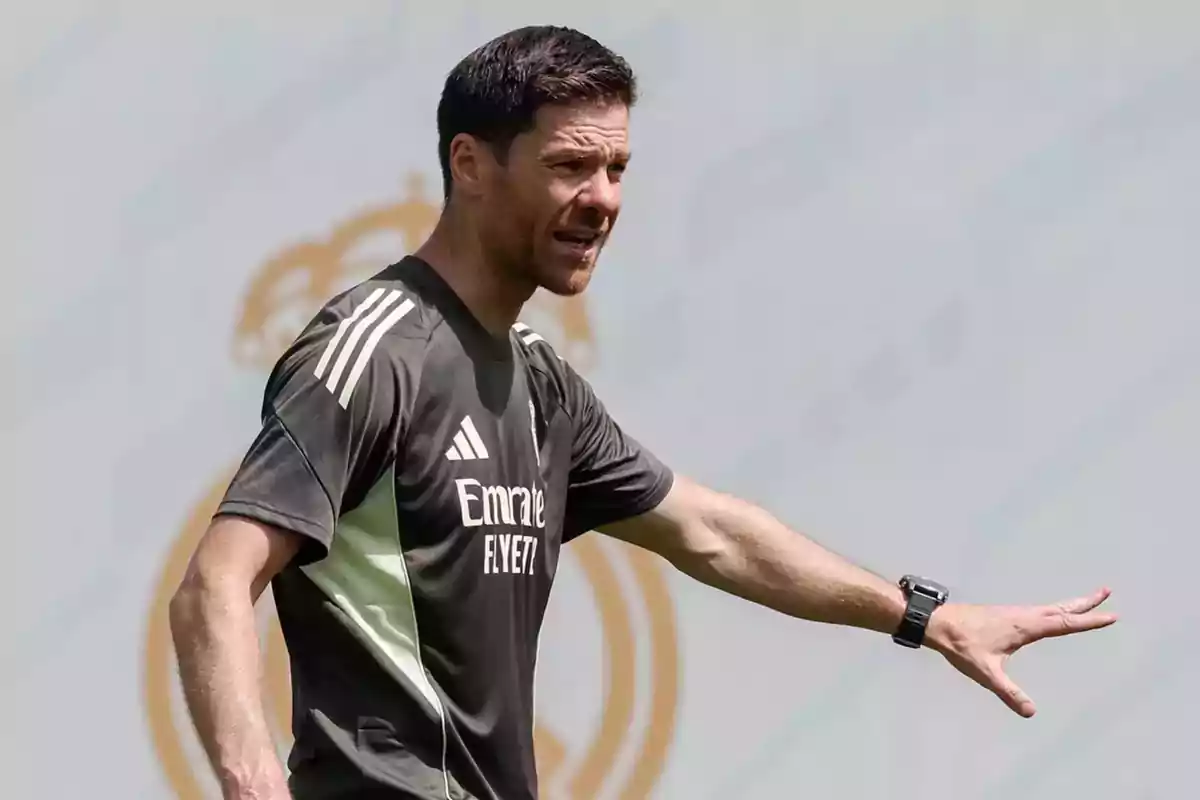 Entrenador de fútbol dando indicaciones en un campo con camiseta de entrenamiento oscura y fondo con el escudo de un club. Entrenador de fútbol dando indicaciones en un campo con camiseta de entrenamiento oscura y fondo con el escudo de un club.