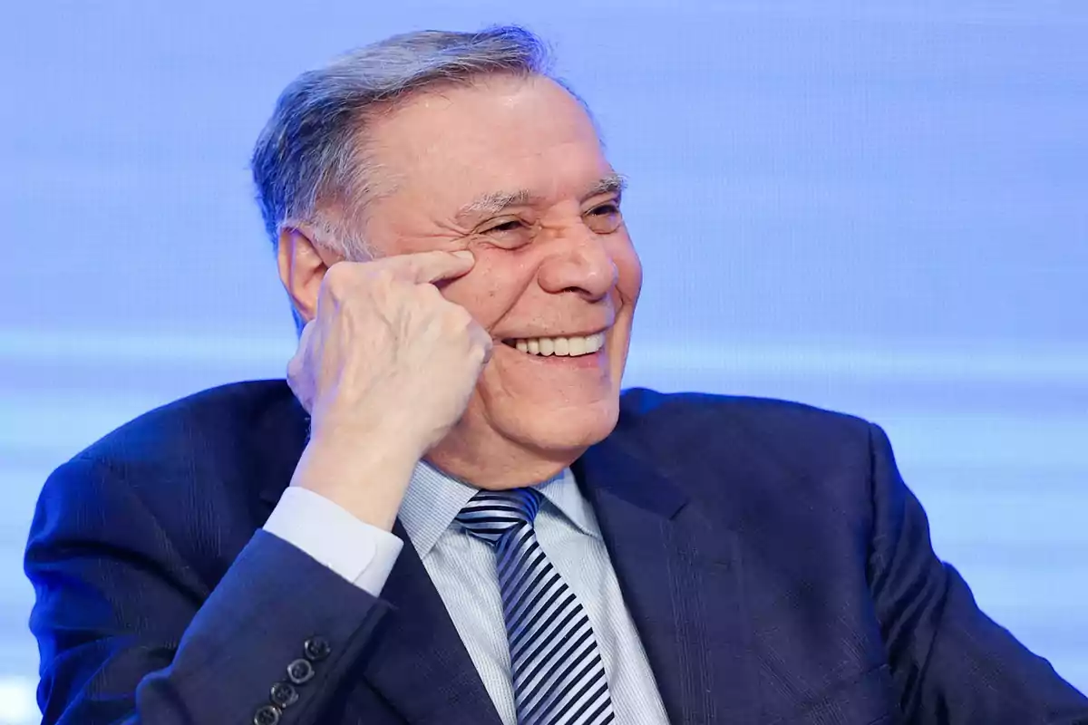 Hombre mayor de cabello canoso sonriendo y usando traje azul con corbata a rayas