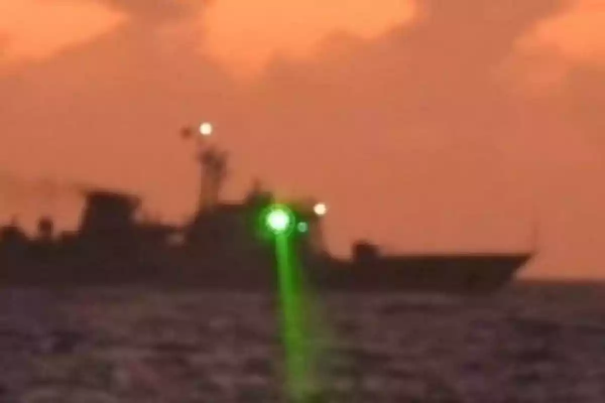 Barco en el mar al atardecer con un haz de luz verde brillante apuntando hacia el agua Barco en el mar al atardecer con un haz de luz verde brillante apuntando hacia el agua