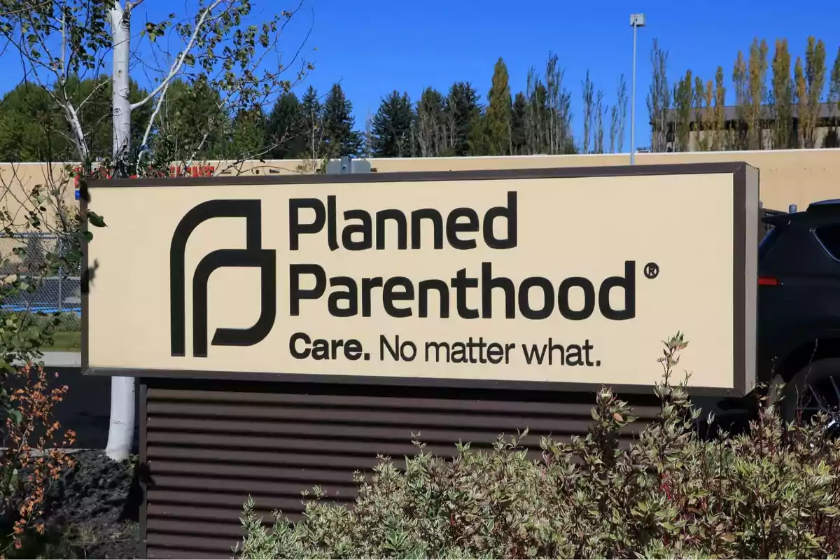 Letrero de Planned Parenthood con el eslogan Care. No matter what. en un entorno exterior con plantas y árboles al fondo Letrero de Planned Parenthood con el eslogan Care. No matter what. en un entorno exterior con plantas y árboles al fondo