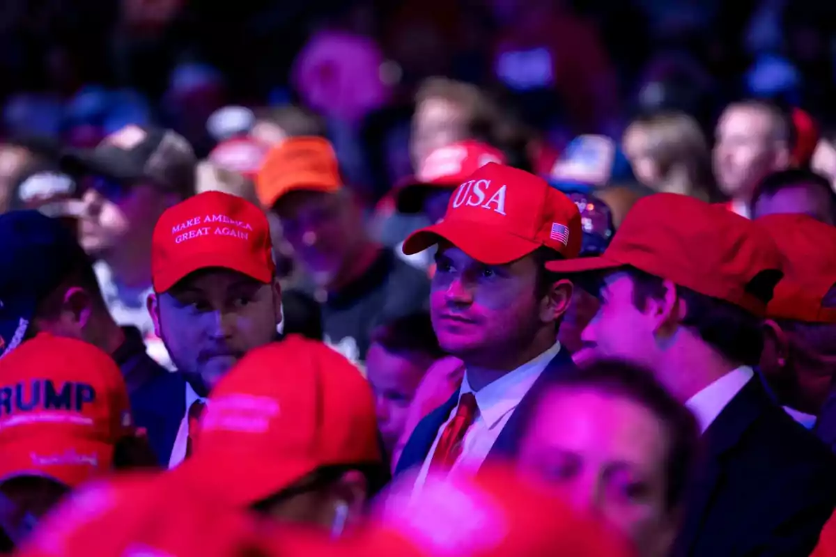Grupo de personas usando gorras rojas con mensajes políticos en un evento multitudinario