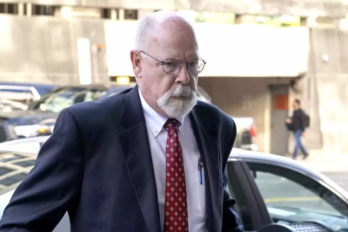 Older man with glasses and a white mustache wearing a dark suit and red tie, walking in an urban area Older man with glasses and a white mustache wearing a dark suit and red tie, walking in an urban area