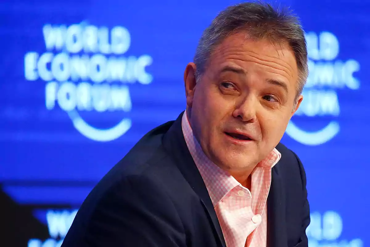 Hombre de mediana edad con camisa rosa y saco oscuro participando en un evento del World Economic Forum con fondo azul Hombre de mediana edad con camisa rosa y saco oscuro participando en un evento del World Economic Forum con fondo azul