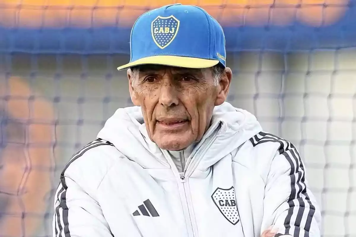 Hombre mayor con gorra azul y campera blanca de Boca Juniors frente a una red de fútbol Hombre mayor con gorra azul y campera blanca de Boca Juniors frente a una red de fútbol