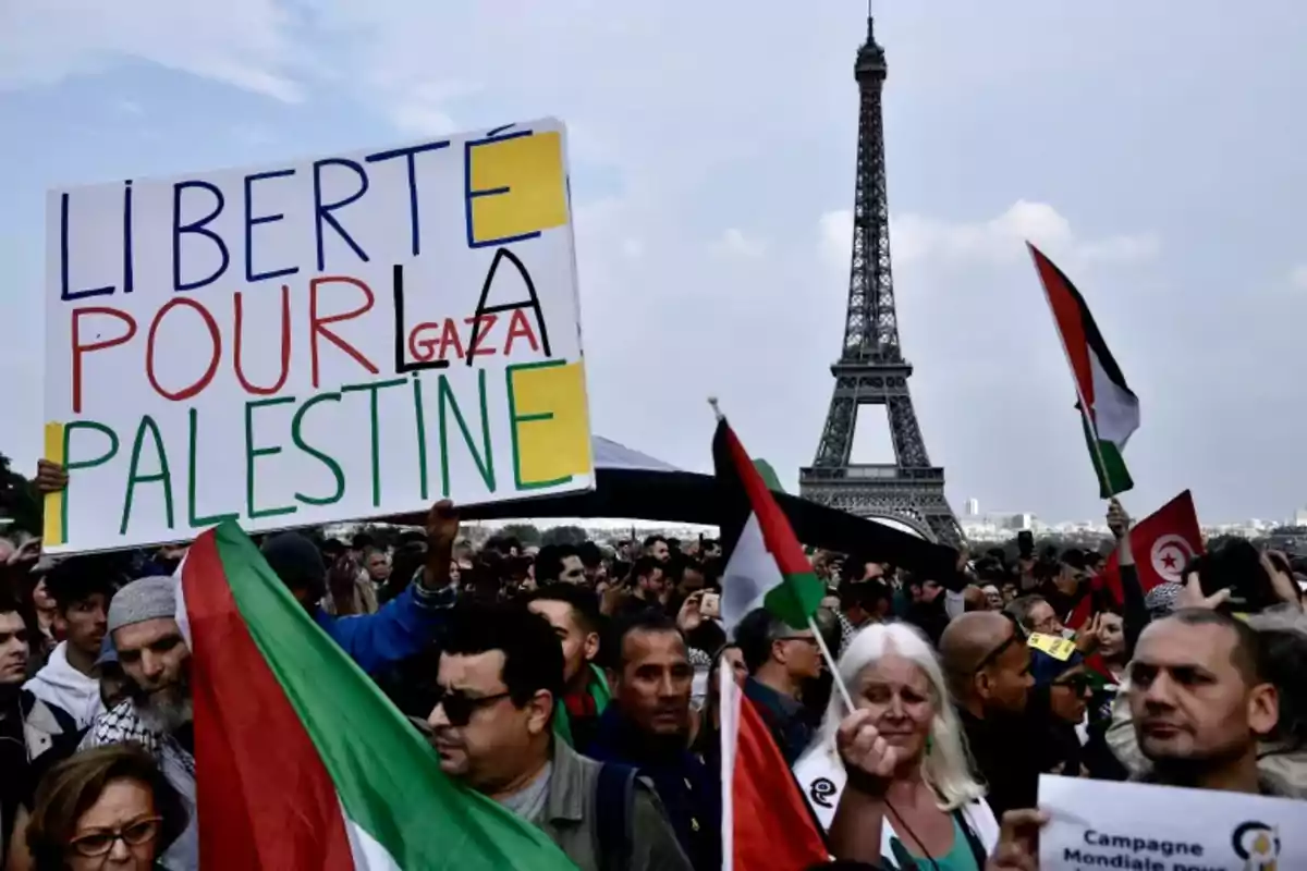 Manifestación en París con personas sosteniendo banderas palestinas y un cartel que pide libertad para Palestina y Gaza, con la Torre Eiffel de fondo. Manifestación en París con personas sosteniendo banderas palestinas y un cartel que pide libertad para Palestina y Gaza, con la Torre Eiffel de fondo.