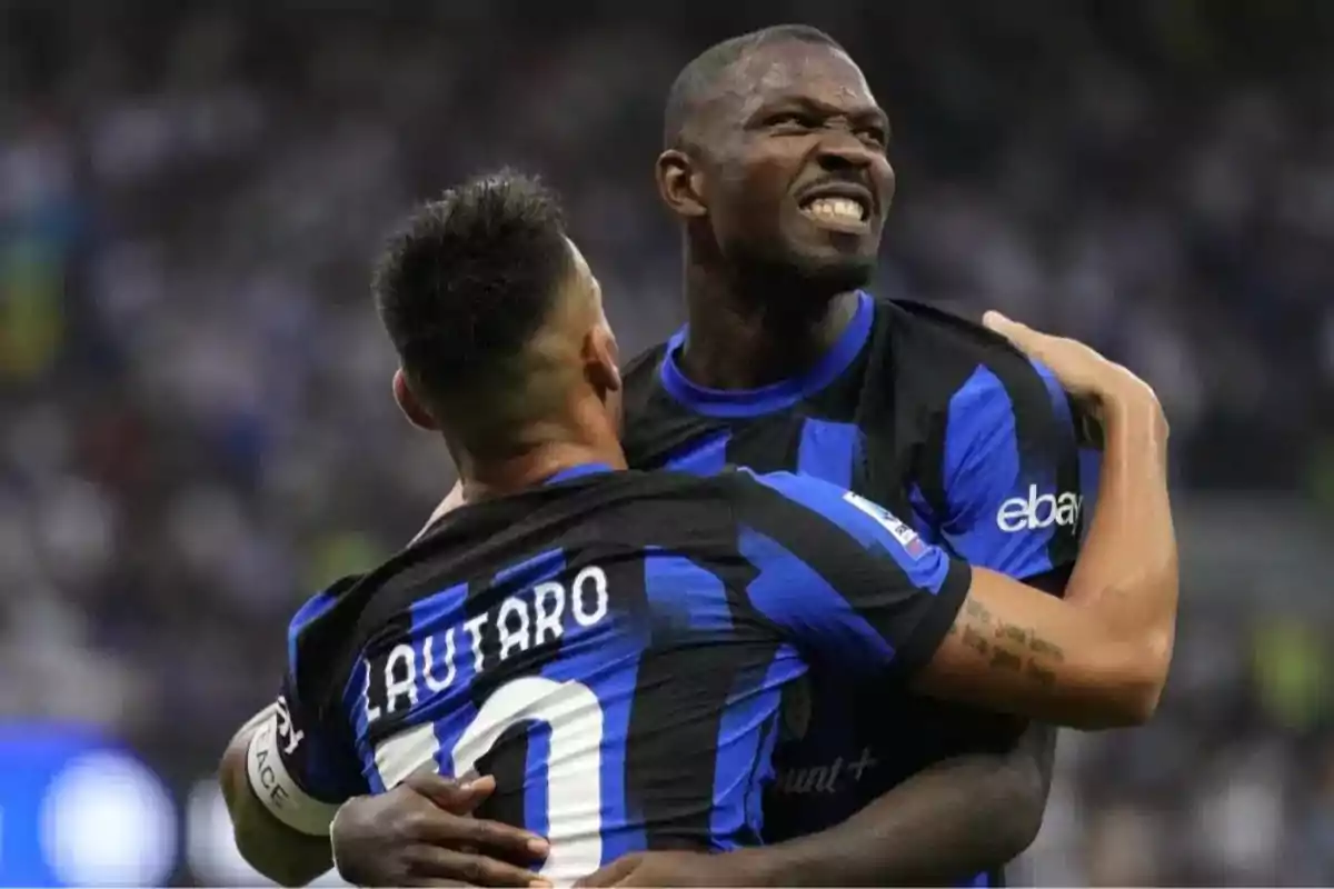 Two Inter Milan players celebrate a goal by hugging on the field; one of them shows an expression of excitement and the other has the name Lautaro on his jersey.