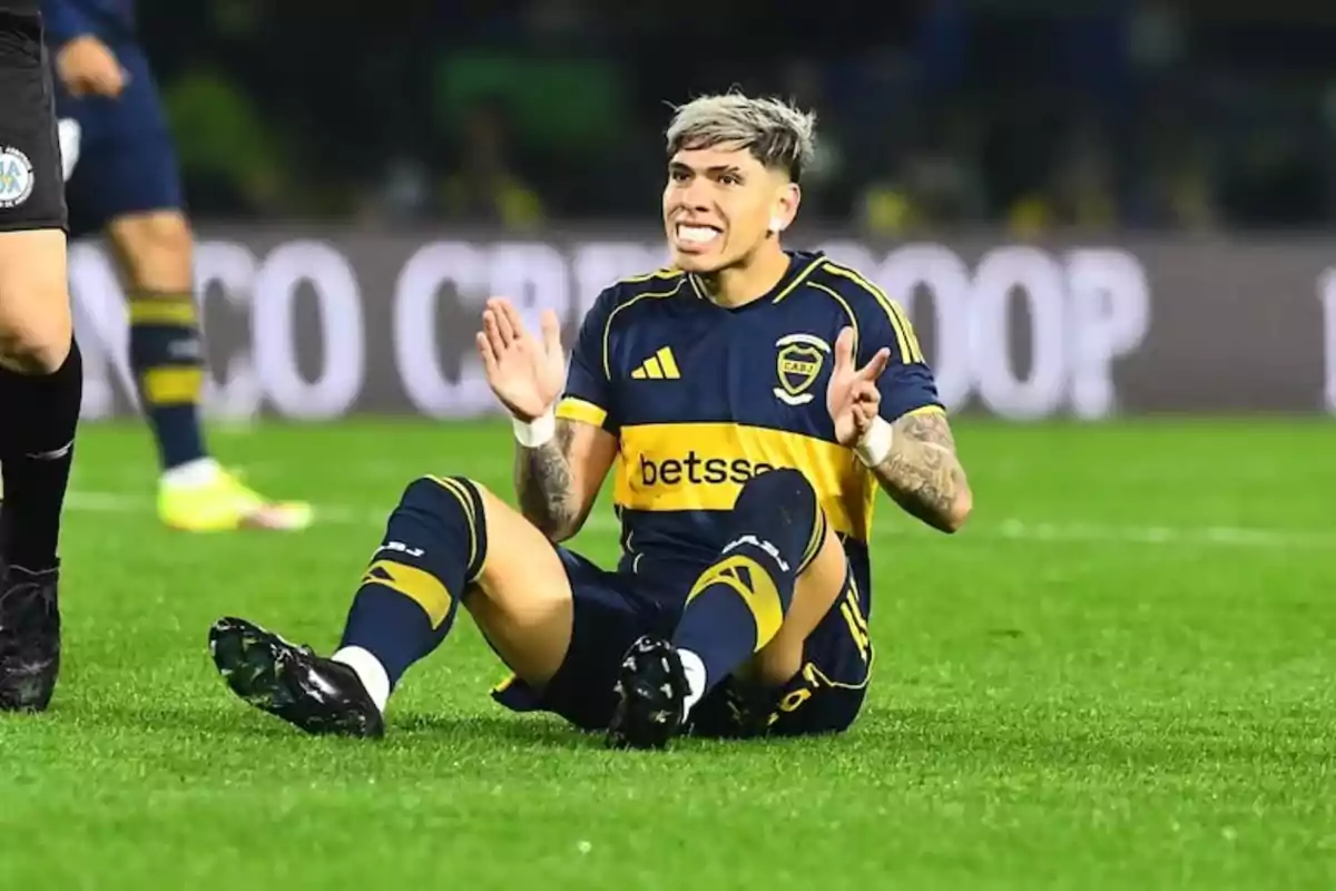 Jugador de fútbol con uniforme azul y amarillo sentado en el césped haciendo un gesto de frustración durante un partido Jugador de fútbol con uniforme azul y amarillo sentado en el césped haciendo un gesto de frustración durante un partido