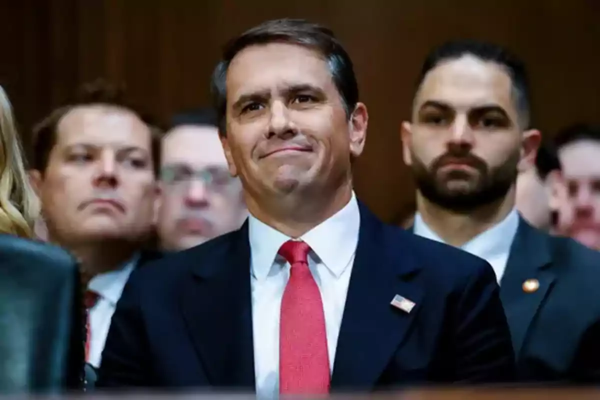 Hombre con traje oscuro y corbata roja sentado entre otras personas en un evento formal Hombre con traje oscuro y corbata roja sentado entre otras personas en un evento formal