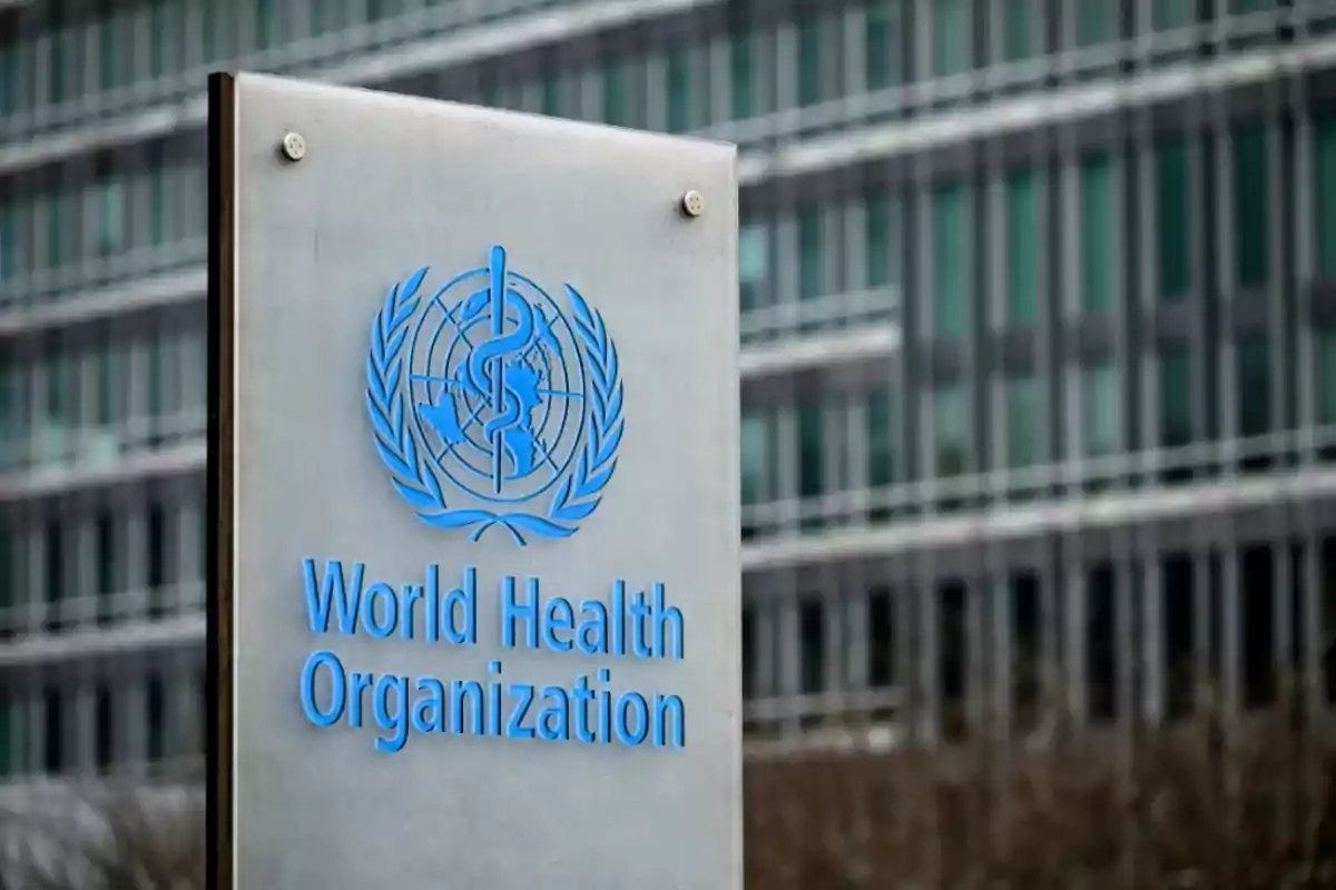 Letrero de la Organización Mundial de la Salud frente a un edificio moderno con ventanas de vidrio Letrero de la Organización Mundial de la Salud frente a un edificio moderno con ventanas de vidrio