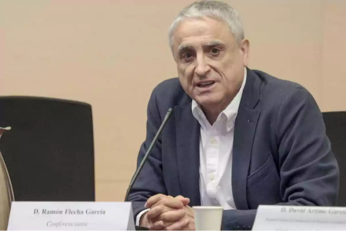 Hombre de cabello canoso y saco azul hablando frente a un micrófono en una conferencia Hombre de cabello canoso y saco azul hablando frente a un micrófono en una conferencia