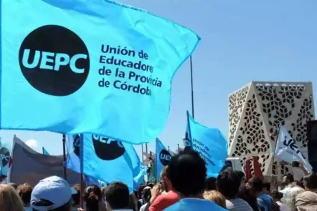 Manifestación de personas con banderas celestes de la Unión de Educadores de la Provincia de Córdoba frente a un edificio moderno en Córdoba Manifestación de personas con banderas celestes de la Unión de Educadores de la Provincia de Córdoba frente a un edificio moderno en Córdoba