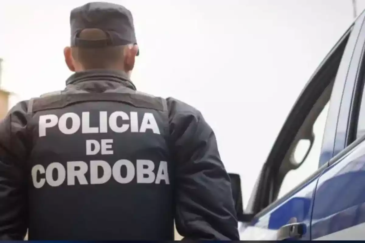 Policía de Córdoba de espaldas junto a un vehículo patrulla Policía de Córdoba de espaldas junto a un vehículo patrulla