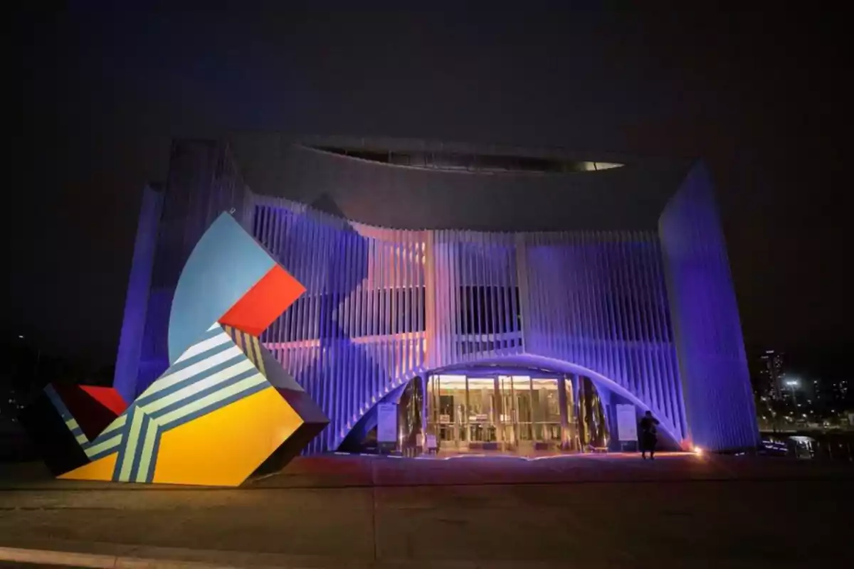 Modern building illuminated by purple lights with a colorful geometric sculpture in the foreground