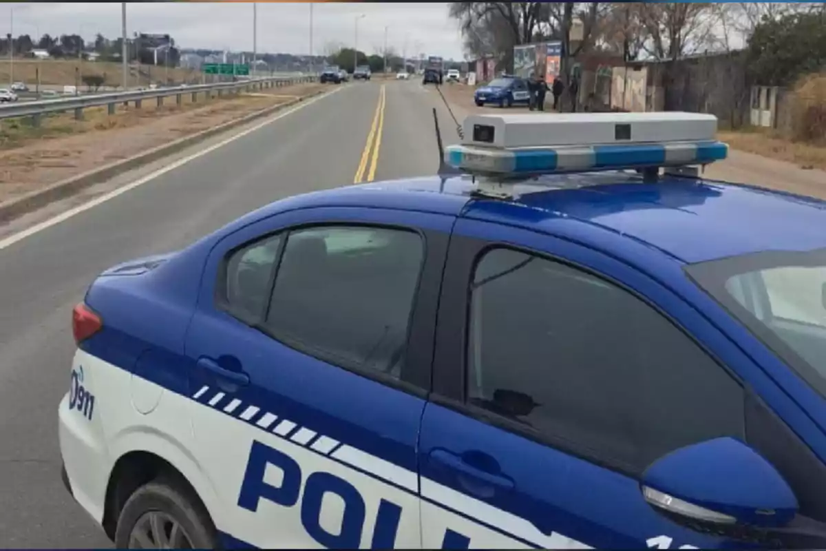 Patrulla policial estacionada en una carretera con otros vehículos y personas al fondo