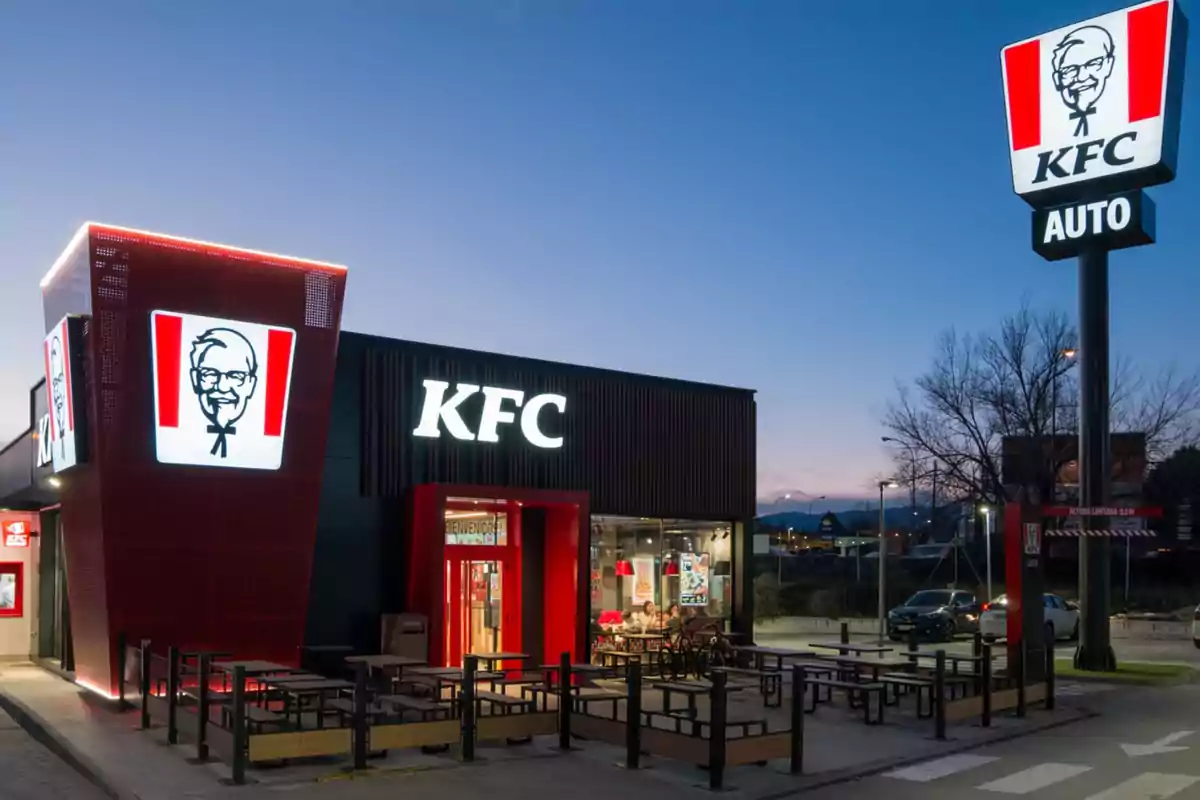 Restaurante de comida rápida KFC con terraza al aire libre y letreros iluminados al atardecer