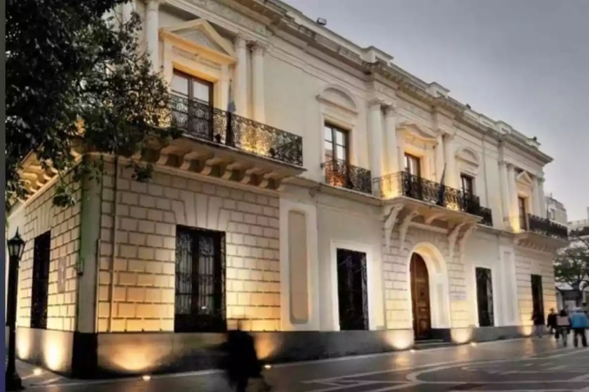 Edificio antiguo de dos pisos con balcones de hierro forjado y fachada iluminada al anochecer en una calle peatonal