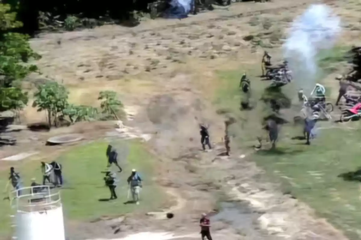 Personas corriendo y levantando polvo en un campo mientras se observa humo en el fondo y varias motocicletas estacionadas Personas corriendo y levantando polvo en un campo mientras se observa humo en el fondo y varias motocicletas estacionadas