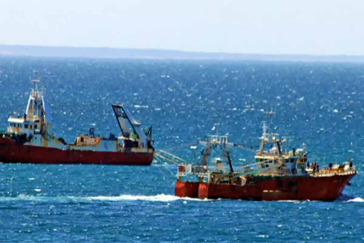 Two red fishing boats sail on the sea under a clear sky