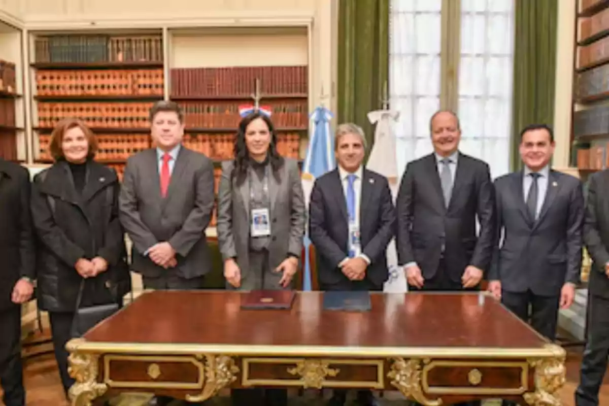 Group of people dressed formally posing behind an elegant desk in a room with bookshelves full of books and flags in the background