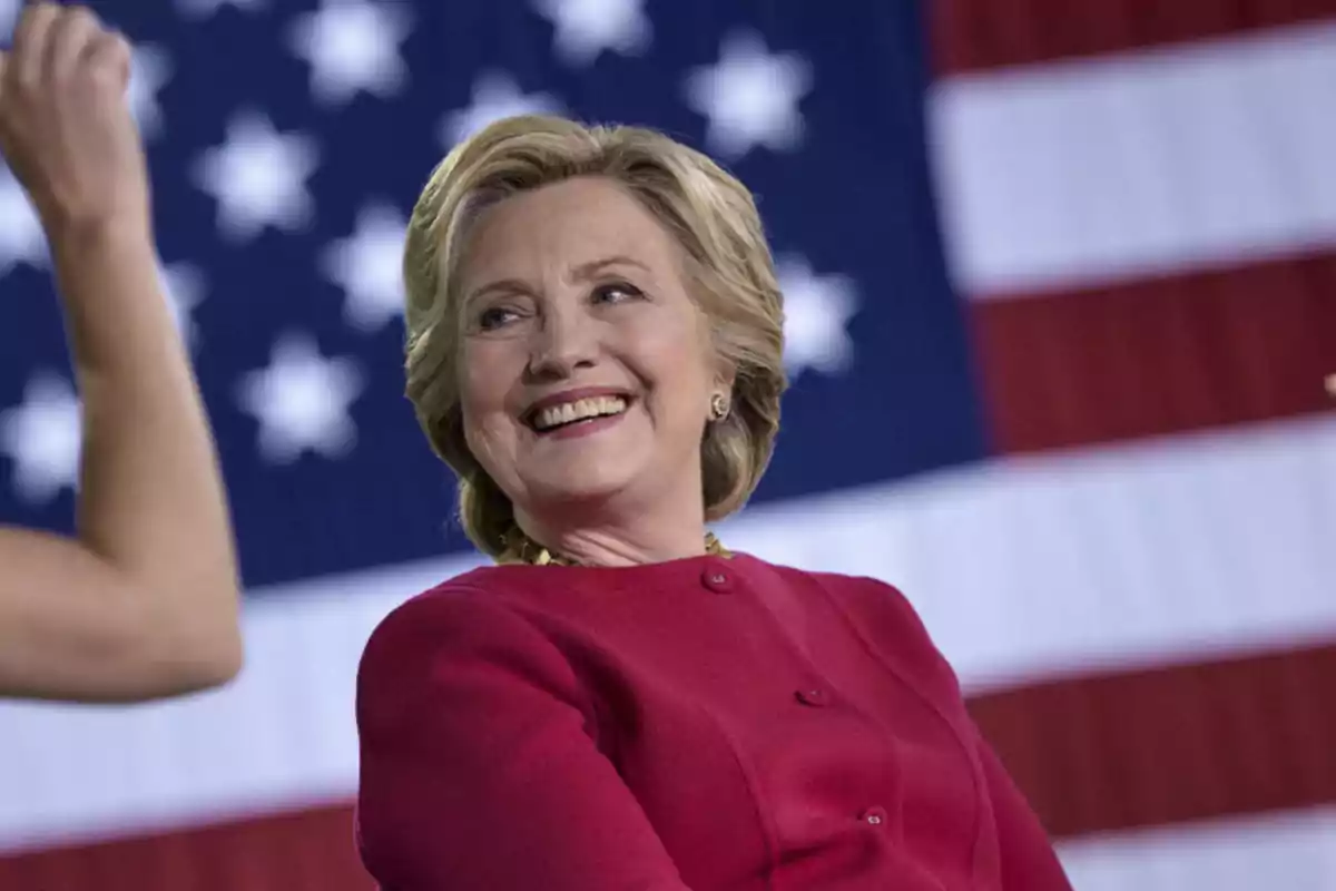 Mujer sonriente con chaqueta roja frente a una bandera de Estados Unidos Mujer sonriente con chaqueta roja frente a una bandera de Estados Unidos